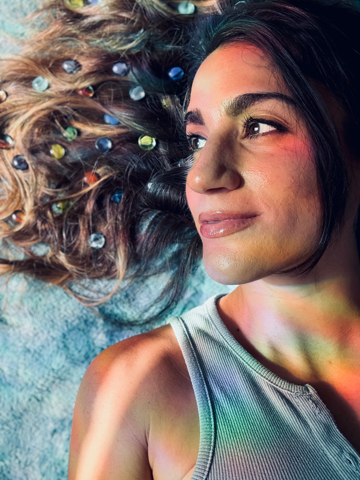 Lauren lying down with colorful gems scattered through her hair, bathed in rainbow light