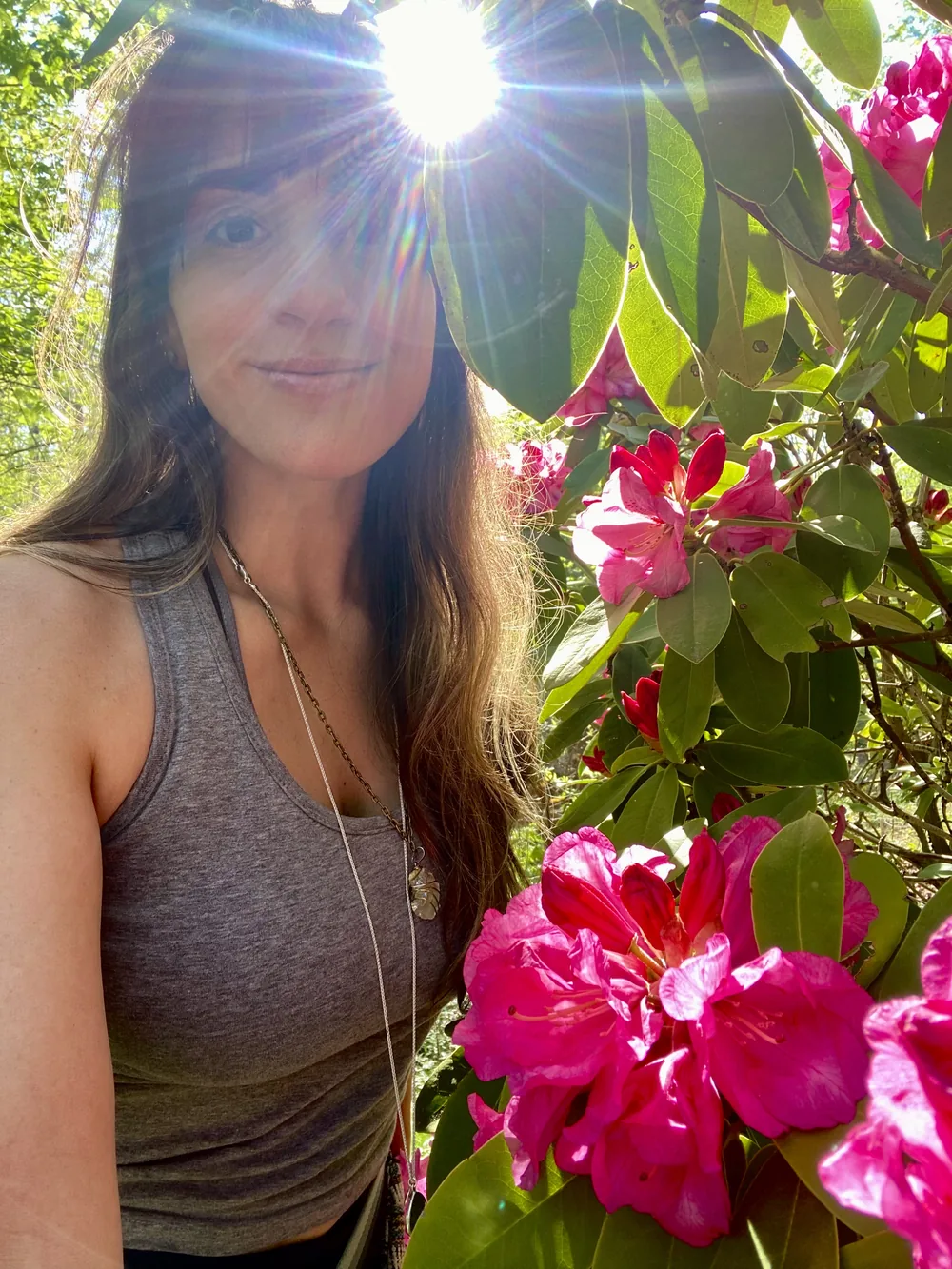 Lauren smiling in the sunshine beside a bush of bright pink rhododendrons